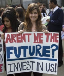 A student holds a sign that reads: 'Aren't we the future? Invest in us!'